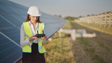 Portrait of a female engineer operating a drone on the background of a solar power plant. Solar panel array installation. Technologies and ecology. Sunsets.