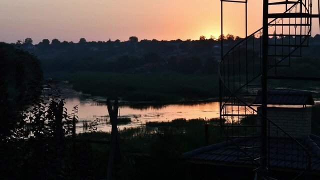 Boat silhouette swim by river at sundown time lapse. Orange sunset sky over Southern Bug river shore with sun reflection in rippled water overgrown by reeds and bulrush plants. Tranquil landscape