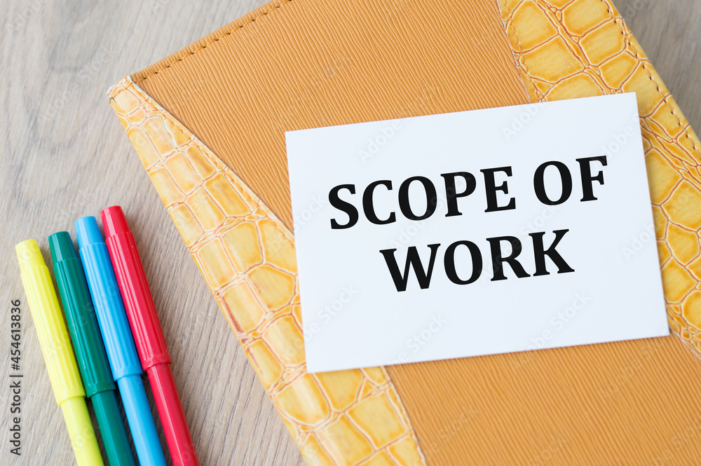 Poster a card with text scope of work on a yellow notebook on the table next to colored markers