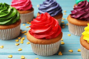 Delicious colorful cupcakes and heart shaped sprinkles on light blue wooden table, closeup