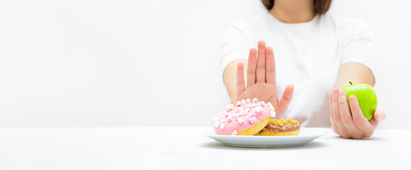Woman on a diet refusing donuts to choose a fresh apple