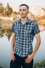 A young man in a plaid shirt at a street photo shoot at sunset, near a pond.