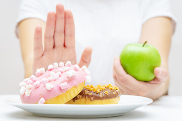 Woman preferring a fresh apple to sweet donuts