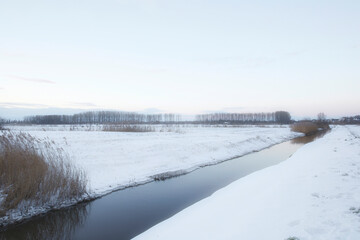 Beautiful winter landscape at sunset with fog and snow covering farmland and river in the Netherlands beautiful colors in nature