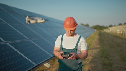 Engineer in hardhat holding tablet computer operating flying drone in solar plant. Photovoltaic solar panel installation. Solar array. New technologies. Portrait of a drone engineer worker