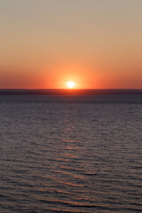 Beautiful colorful sunset over the sea. The red sun and the absence of clouds. Sea horizon. Aerial view. Landscape. The concept of a postcard picture. Light waves on the sea surface