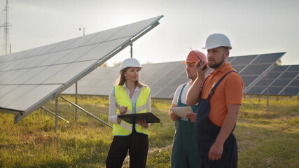 Three solar energy specialists at a solar power facility. Professional engineers discuss innovative...