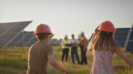 Two small children run to their parents who are at work. A solar power plant employee with children at work smiling at the camera. Three solar energy specialists at a solar power facility.