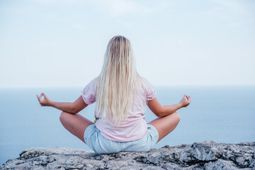 Fototapeta na wymiar A long blonde haired girl meditating on the cliff over the ocean