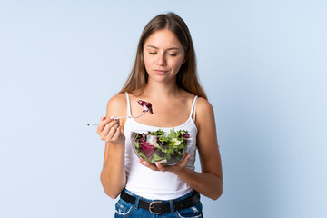 Young Lithuanian woman isolated on blue background holding a bowl of salad with sad expression