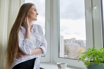 Portrait of young woman with cup of coffee near winter autumn window