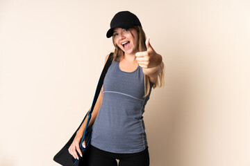 Young sport Lithuanian woman holding a sport bag isolated on beige background with thumbs up because something good has happened