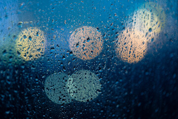 Wet window glass with raindrops and bokeh light of unfocused night city behind.