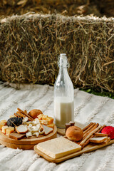 Vertical cheese assortment on wooden board with milk and bread in front of dried grass straw