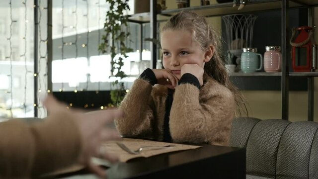 a little girl with blonde hair laughs sitting in a cafe and talking to someone. High quality FullHD footage