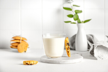 cookies and milk in a glass on a white table with a napkin and little vase
