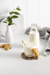 Fototapeta na wymiar cookies and milk in a glass and bottle on a white table with a napkin and little vase