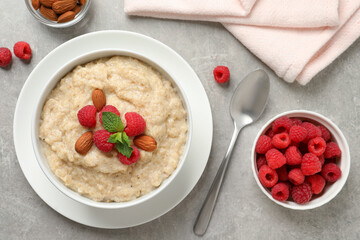 Tasty oatmeal porridge with raspberries and almond nuts served on light grey table, flat lay