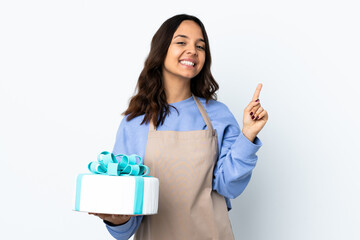 Pastry chef holding a big cake over isolated white background showing and lifting a finger in sign of the best