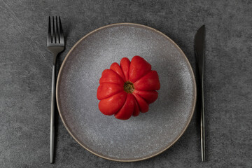 Red ripe tomato on a gray platter. Minimalistic table setting in dark colours. Healthy food concept. World Vegetarian Day.