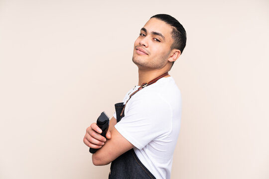 Hairdresser man in an apron isolated on beige background laughing