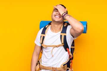 Young mountaineer asian man with a big backpack isolated on yellow background laughing