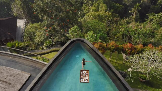 aerial view woman having breakfast in swimming pool enjoying exotic food at luxury hotel spa with view of tropical jungle