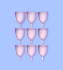 Many purple menstrual cups on light blue background, flat lay