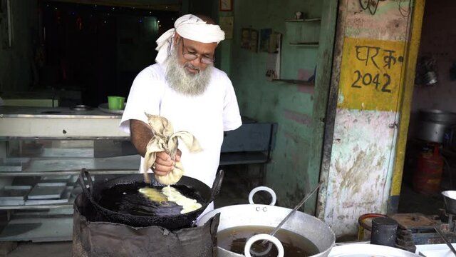 Indian villager man making jalebi sweet dish in a big oil pan, India