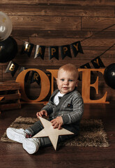 Fototapeta na wymiar a little birthday boy in a gray suit is sitting on a festive background