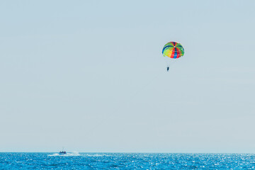 Extreme sports and exciting rest. Tourists fly on parashute in the blue sky above the sea and the horizon line