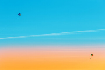 Extreme sports and exciting rest. Two tourists fly on a parashute in the blue sky and sunset background
