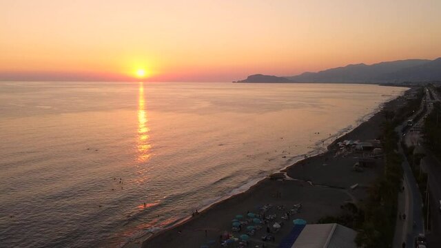 Aerial view of coastal motorway, beach and sun setting behind mediterranean sea horizon. Beautiful seaside sunset. Mahmutlar, Antalya, Turkey