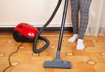 Housewife cleans the floor with a vacuum cleaner.