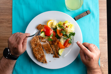 male hand eating from big dish German schnitzel with salad