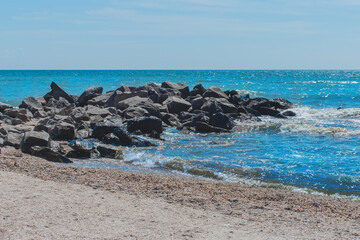 Breakwater beach stones on the sea coast with small waves and blue water against the background of the horizon line