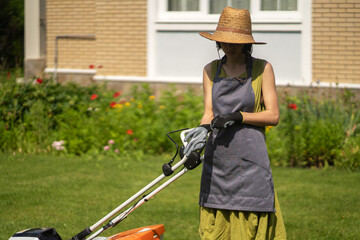 A girl is mowing a lawn in the backyard with an orange lawn mower