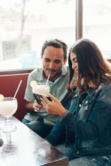 Latin couple haven fun wacthing funny videos at the phone at the restaurant