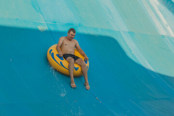 A young man on an inflatable ring in a water park. A man on a yellow inflatable circle on a steep...