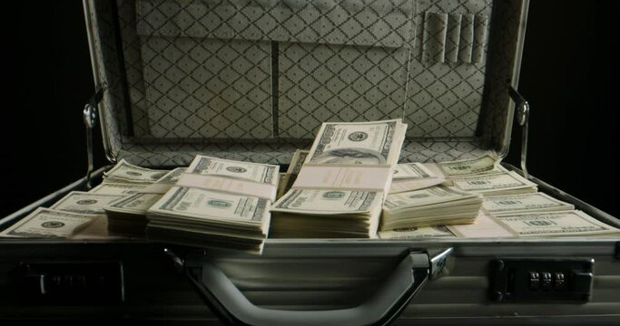 Packs of cash falling into a metal case filled with money. 100 dollar bills in a briefcase. Finance, investing, business concept close up 4k footage