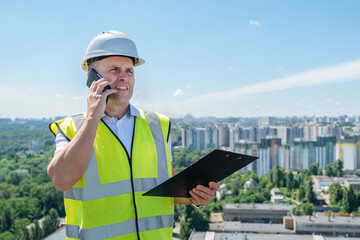 Portrait of a mature man in white helmet at construction site, who checks the schedule while...
