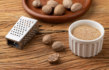 Nutmegs with grater over wodden table. Nuts in a bowl