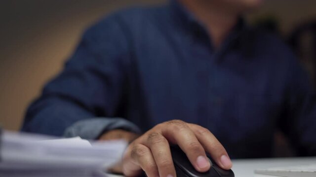 Young asian businessman working with computer in the dark office at night. Attractive Indian man work hard overtime in home with floor lamp ambient warm light late at night
