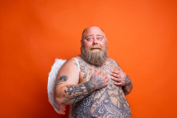 Fat amazed man with beard ,tattoos and wings acts like an angel