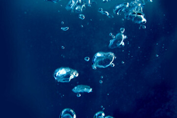 Naklejka na ściany i meble big and small air bubbles rise in the water from the bottom to the surface, blue background, concept sparkling water, drown, breathing underwater