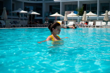 Naklejka premium young female person in yellow swimsuit swimming in the pool, summer resort vacation