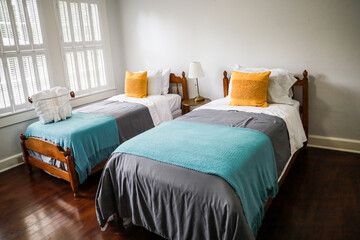 A guest bedroom with two twin beds with turquoise and gray bedspreads and yellow decorative pillows - obrazy, fototapety, plakaty