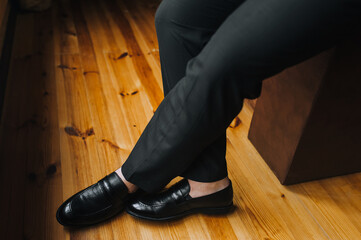 Legs of a man of a businessman in trousers and black shiny shoes on a background of wooden parquet. Business photography.