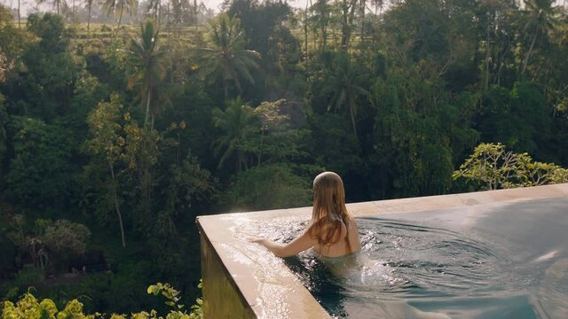 happy woman relaxing in swimming pool enjoying vacation lifestyle at luxury hotel spa looking at view of tropical jungle at sunrise 4k