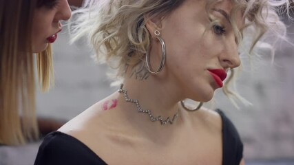 Close-up loving sensual lesbian woman kissing partner on neck and cheek leaving red lipstick on skin. Passionate young Caucasian LGBT couple enjoying leisure together indoors. Love and diversity